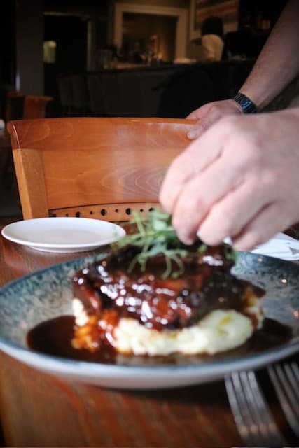 A plated meat dish finished with sauce and herbs